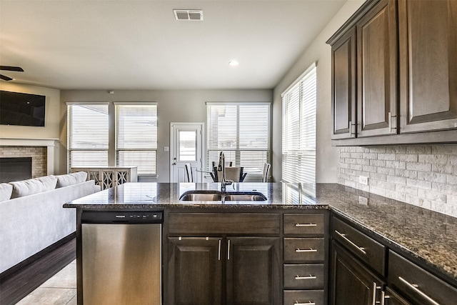 kitchen featuring a sink, visible vents, open floor plan, stainless steel dishwasher, and dark stone countertops