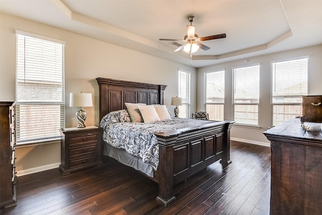 bedroom with dark wood-style floors, a tray ceiling, ceiling fan, and baseboards