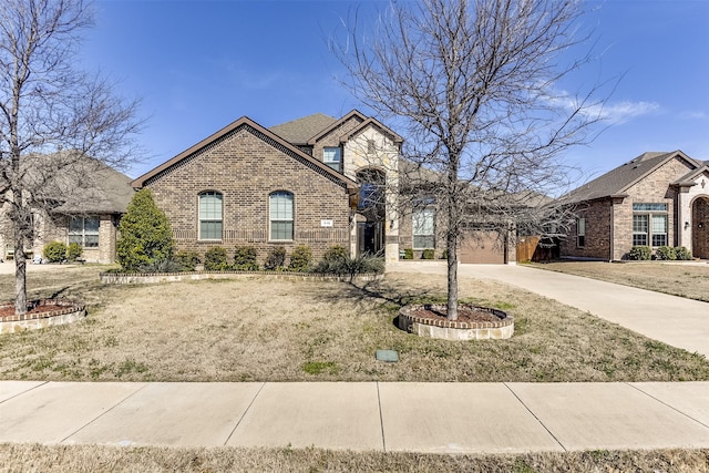 french country home with driveway, an attached garage, a front lawn, and brick siding