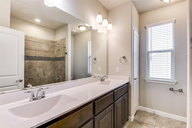 bathroom with double vanity, tiled shower, a sink, and baseboards