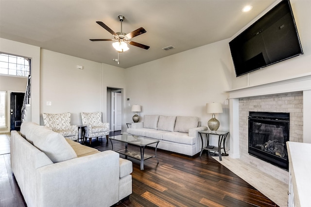 living room with a ceiling fan, a fireplace, visible vents, and dark wood-style flooring