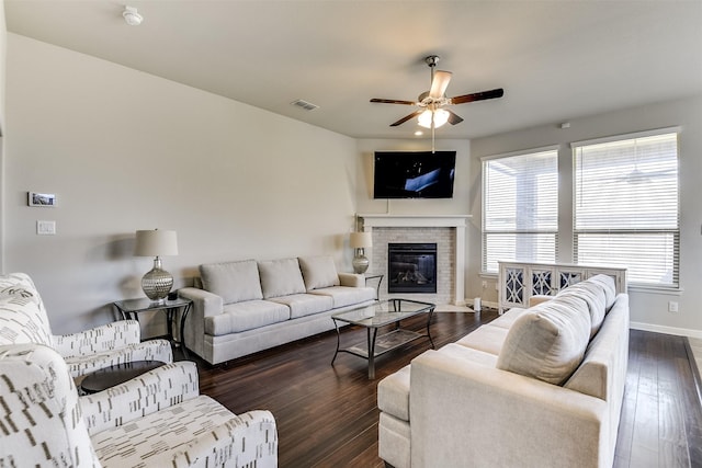 living area with baseboards, visible vents, a glass covered fireplace, ceiling fan, and dark wood-style flooring