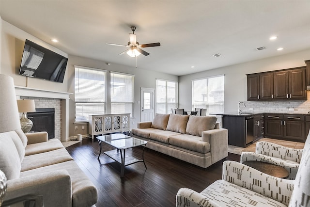 living room with dark wood-style flooring, recessed lighting, visible vents, a brick fireplace, and ceiling fan