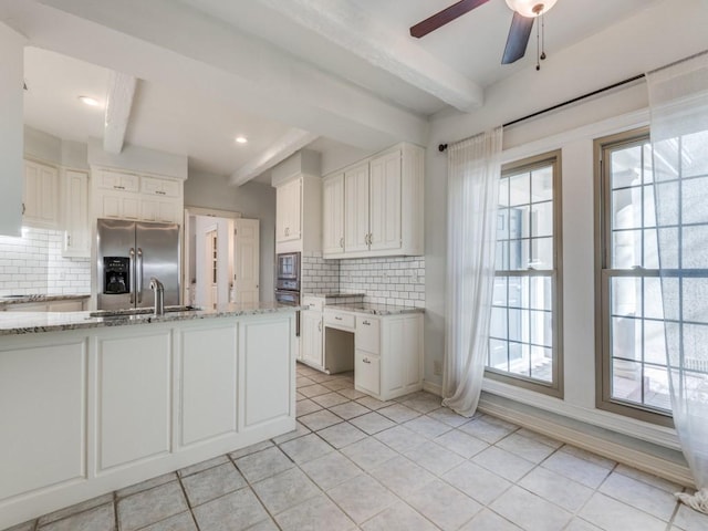 kitchen with appliances with stainless steel finishes, beam ceiling, white cabinetry, and light stone counters