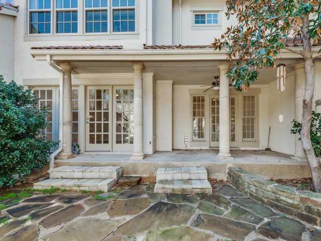 entrance to property with stucco siding, a porch, a ceiling fan, and a tiled roof