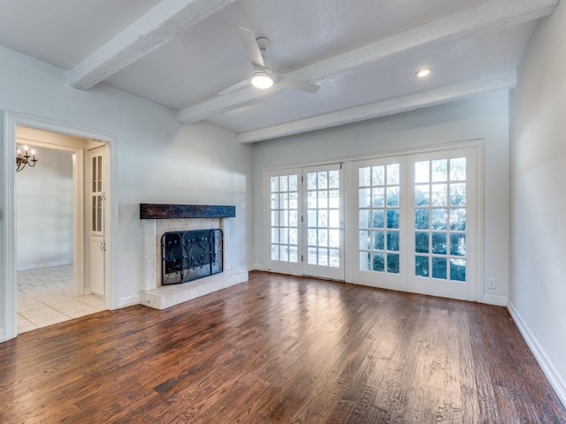 unfurnished living room featuring baseboards, a high end fireplace, light wood-style floors, beam ceiling, and ceiling fan with notable chandelier