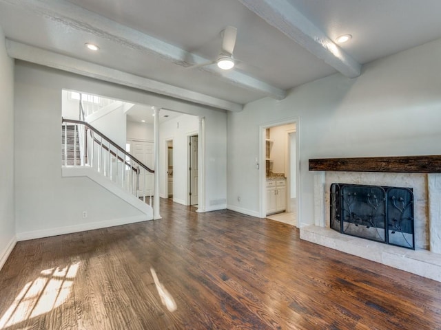 unfurnished living room with baseboards, a fireplace with raised hearth, wood finished floors, stairs, and beam ceiling