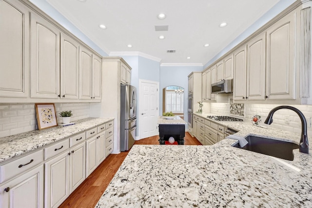 kitchen featuring arched walkways, light stone counters, stainless steel appliances, wood finished floors, and a sink