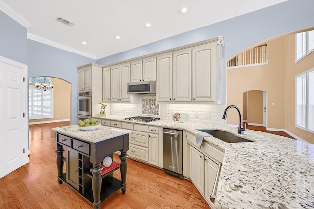 kitchen with arched walkways, a sink, appliances with stainless steel finishes, cream cabinetry, and light stone countertops