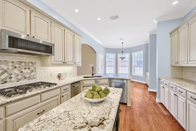 kitchen with hanging light fixtures, appliances with stainless steel finishes, a sink, and cream cabinetry