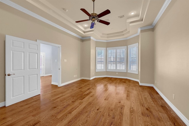 unfurnished room with light wood-style floors, a raised ceiling, and ornamental molding