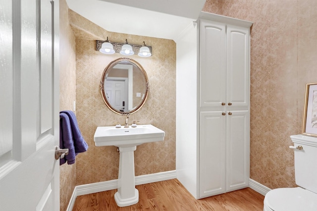 bathroom with wallpapered walls, wood finished floors, toilet, and baseboards