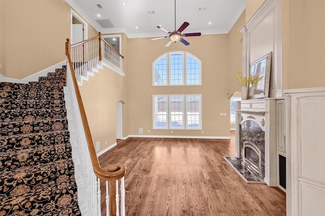 living area featuring light wood-style flooring, a towering ceiling, a high end fireplace, stairs, and crown molding