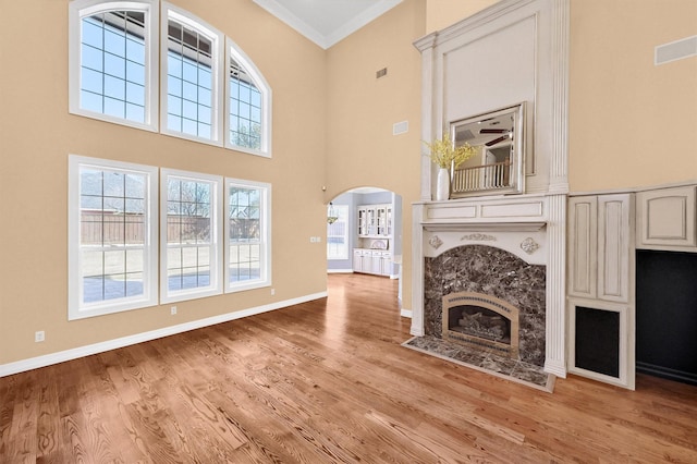 unfurnished living room with light wood-type flooring, baseboards, arched walkways, and crown molding