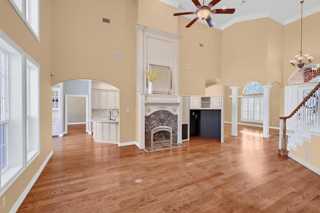 unfurnished living room featuring arched walkways, decorative columns, light wood-style flooring, a premium fireplace, and ceiling fan with notable chandelier