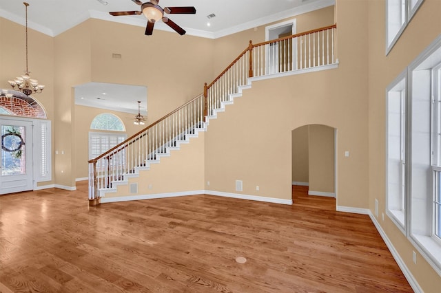 foyer entrance featuring baseboards, ornamental molding, wood finished floors, stairs, and ceiling fan with notable chandelier