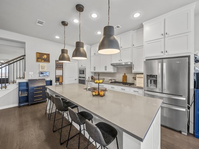 kitchen featuring a kitchen breakfast bar, hanging light fixtures, stainless steel appliances, under cabinet range hood, and white cabinetry