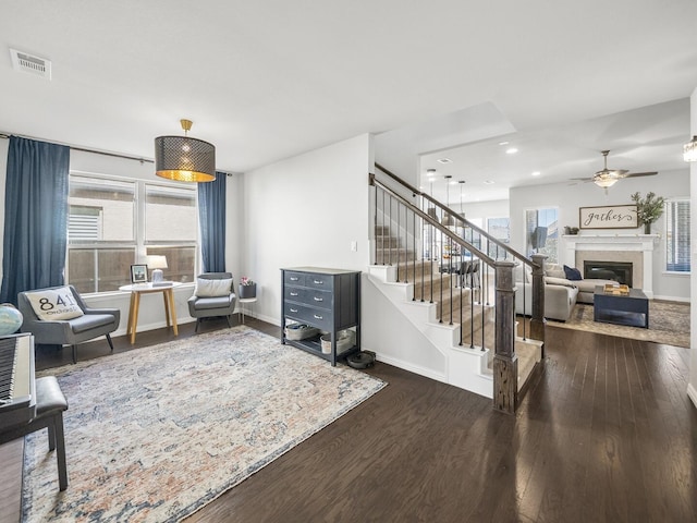 living area featuring baseboards, visible vents, a glass covered fireplace, dark wood-style floors, and stairway