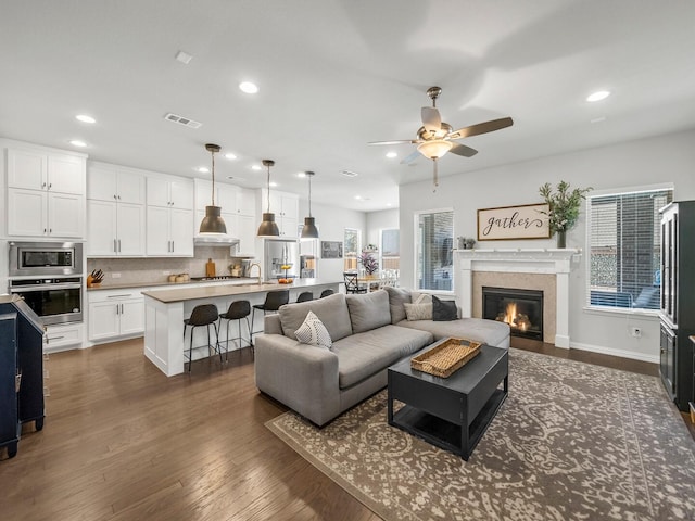 living room featuring ceiling fan, recessed lighting, visible vents, dark wood-style floors, and a glass covered fireplace