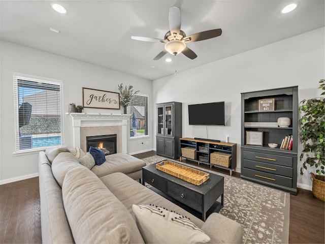 living room with dark wood-style floors, recessed lighting, ceiling fan, a lit fireplace, and baseboards