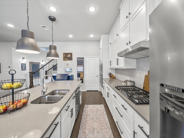 kitchen with under cabinet range hood, a sink, white cabinets, hanging light fixtures, and appliances with stainless steel finishes