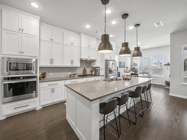 kitchen with visible vents, white cabinets, appliances with stainless steel finishes, an island with sink, and pendant lighting