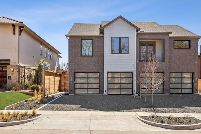 view of front of house featuring gravel driveway, an attached garage, a shingled roof, and brick siding