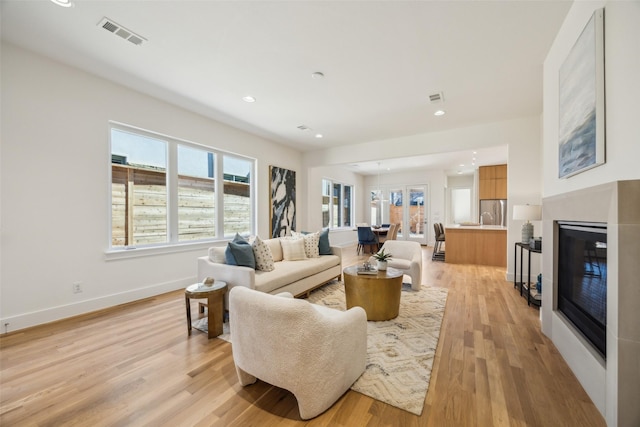 living area with baseboards, a glass covered fireplace, visible vents, and light wood-style floors