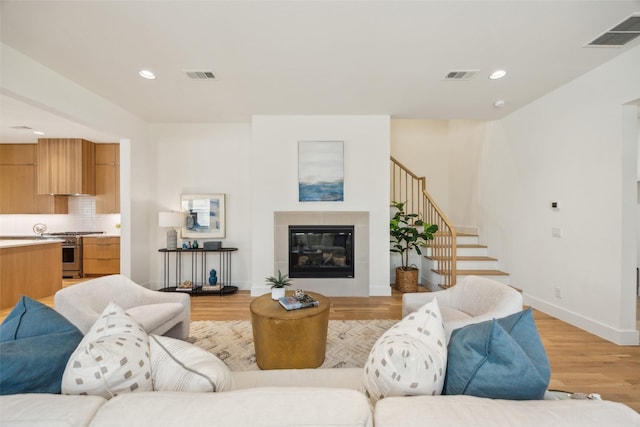 living room featuring light wood-style flooring, a glass covered fireplace, and visible vents