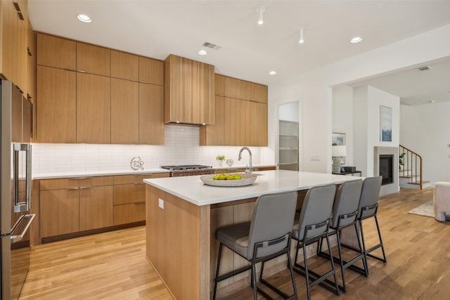 kitchen with built in fridge, a kitchen island with sink, light countertops, light wood finished floors, and modern cabinets