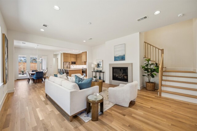 living area featuring light wood-type flooring, visible vents, a glass covered fireplace, and stairs