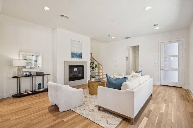 living area with light wood-style flooring, a glass covered fireplace, visible vents, and recessed lighting