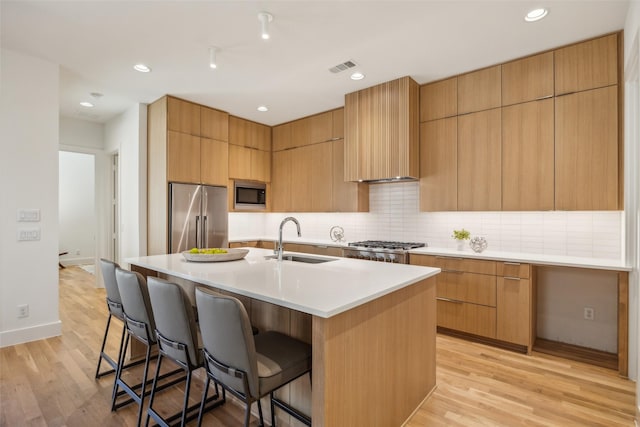 kitchen with an island with sink, stainless steel appliances, a sink, and light countertops