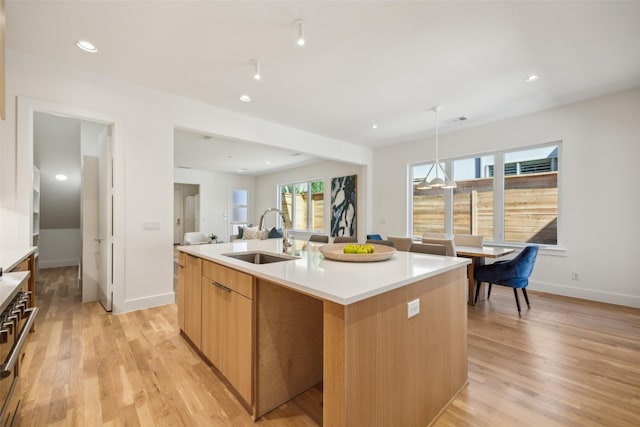 kitchen with a center island with sink, light countertops, light wood-type flooring, pendant lighting, and a sink