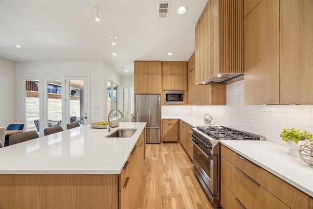 kitchen with light countertops, appliances with stainless steel finishes, a sink, and a large island with sink