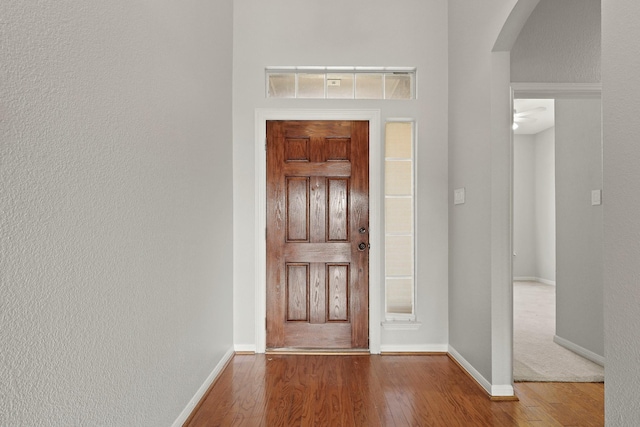 foyer entrance with arched walkways, a textured wall, baseboards, and wood finished floors