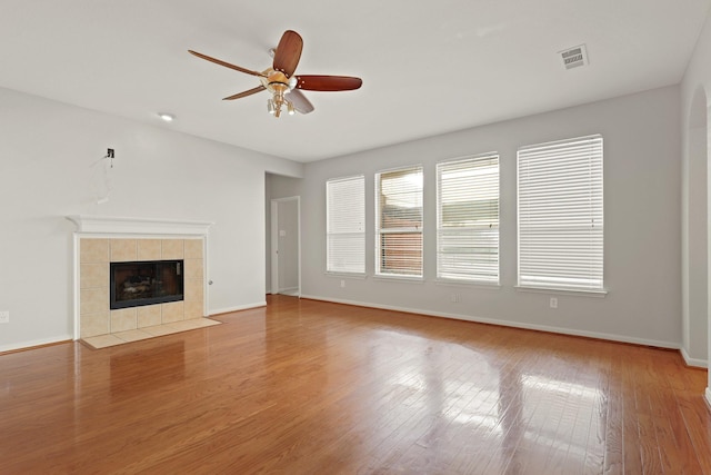 unfurnished living room with baseboards, visible vents, a ceiling fan, a tile fireplace, and wood finished floors