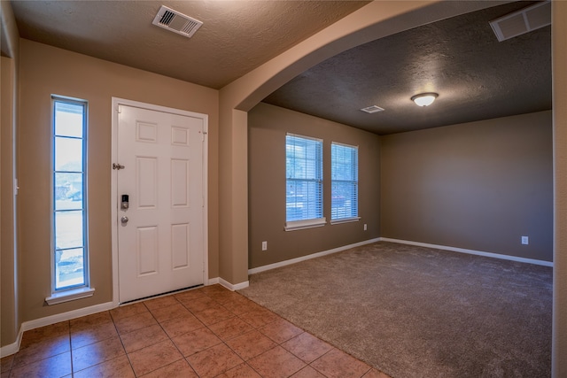 entryway featuring light colored carpet, arched walkways, visible vents, and a textured ceiling