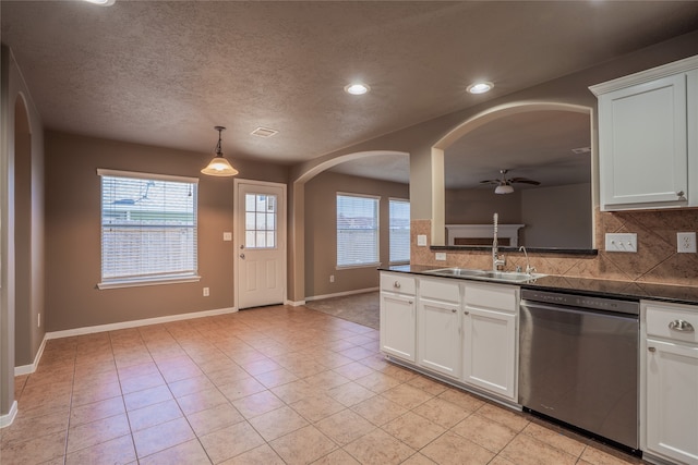 kitchen with stainless steel dishwasher, dark countertops, a sink, and white cabinetry