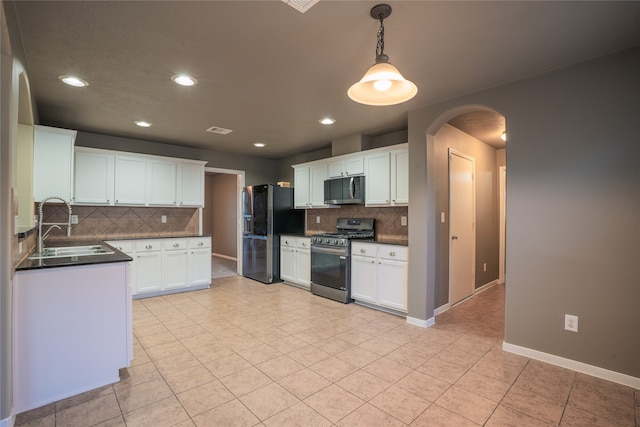 kitchen featuring arched walkways, white cabinets, dark countertops, stainless steel appliances, and a sink