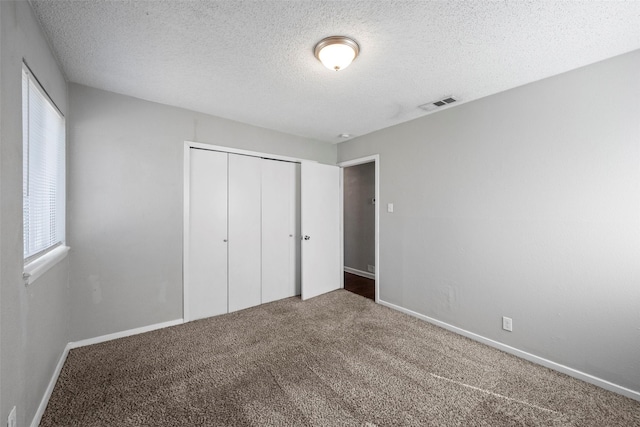 unfurnished bedroom with baseboards, visible vents, carpet, a textured ceiling, and a closet