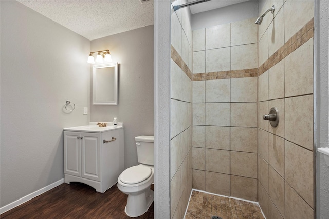 bathroom featuring toilet, wood finished floors, a tile shower, a textured ceiling, and vanity