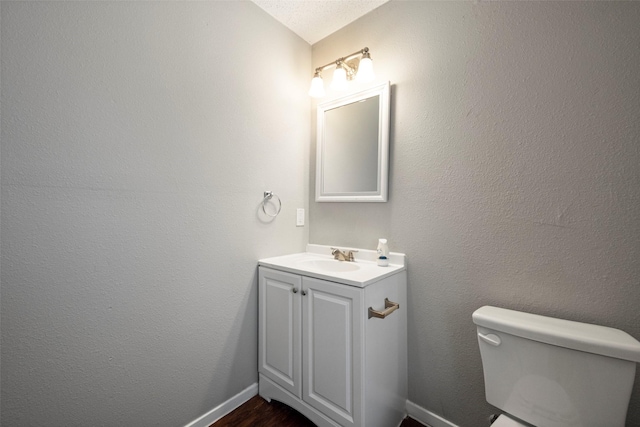 bathroom featuring baseboards, a textured wall, toilet, vaulted ceiling, and vanity