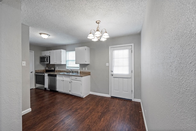 kitchen with stainless steel appliances, a sink, white cabinetry, dark wood-style floors, and decorative light fixtures