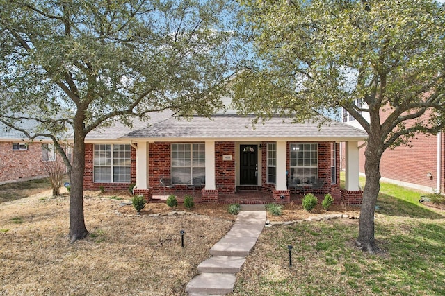 view of front of house featuring roof with shingles, a front lawn, a porch, and brick siding