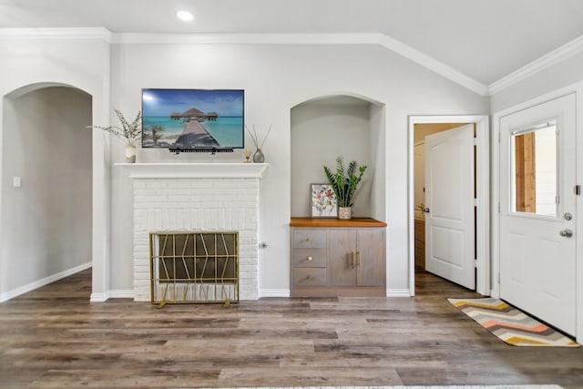 unfurnished living room featuring baseboards, wood finished floors, vaulted ceiling, crown molding, and a fireplace