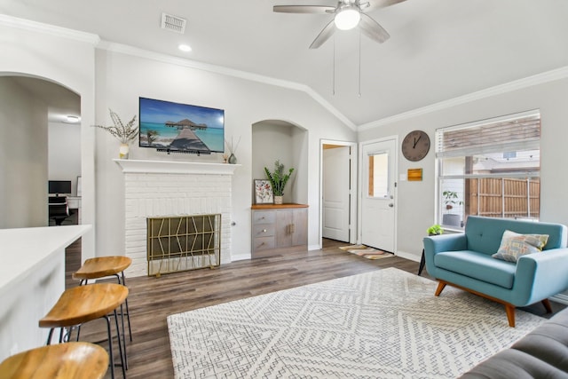 living area with crown molding, visible vents, a brick fireplace, vaulted ceiling, and wood finished floors