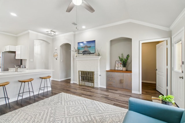 living room featuring visible vents, lofted ceiling, ornamental molding, dark wood-type flooring, and a brick fireplace