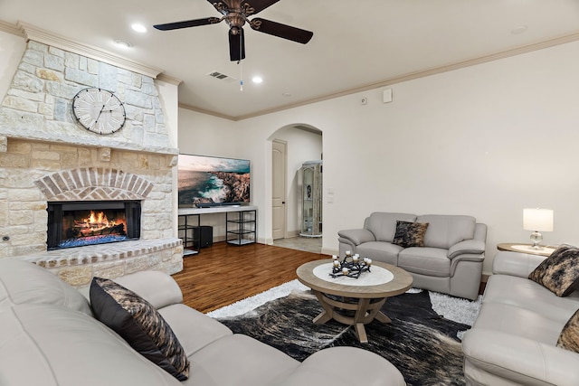 living area featuring arched walkways, visible vents, ornamental molding, a stone fireplace, and wood finished floors