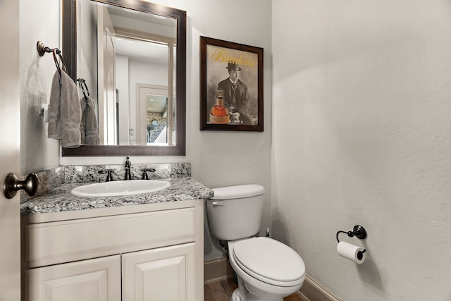 bathroom featuring baseboards, a textured wall, vanity, and toilet